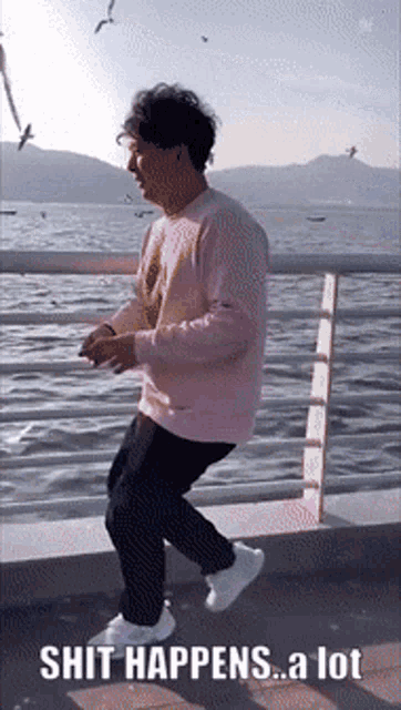 a man in a pink sweater is dancing in front of a body of water
