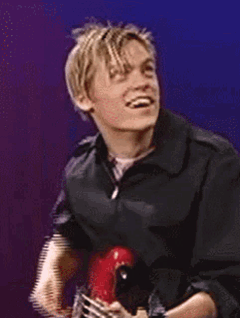 a man in a black jacket holds a red guitar