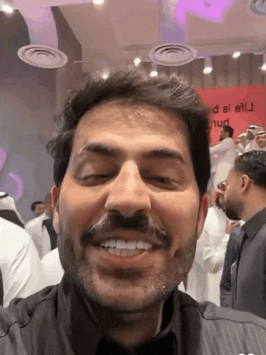 a man with a beard is smiling with his eyes closed in front of a crowd