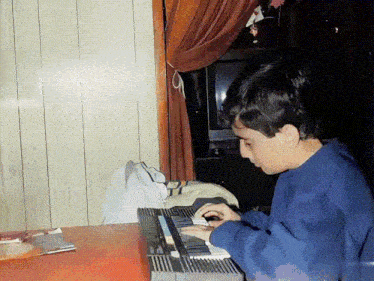 a young boy in a blue sweatshirt is playing a keyboard