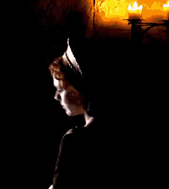 a woman is standing in the dark with a candle in the background
