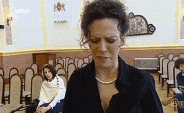 a woman with a pearl necklace is standing in a room with other women .