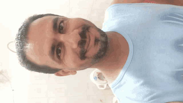 a man with a beard is smiling and wearing a blue tank top