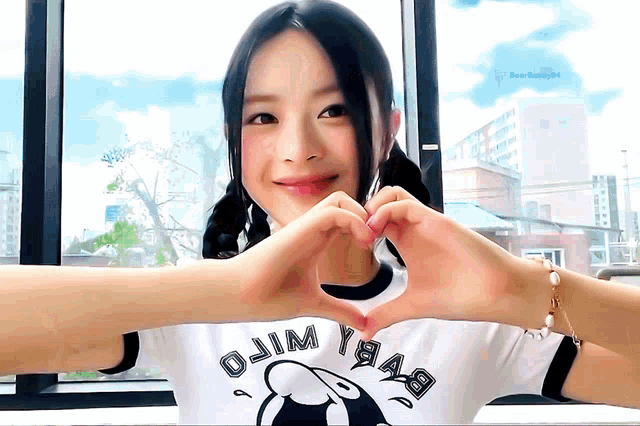a woman making a heart shape with her hands wearing a shirt that says ojim yaas