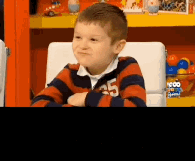 a young boy is sitting in a chair with his arms crossed and wearing a striped shirt with the number 25 on it .