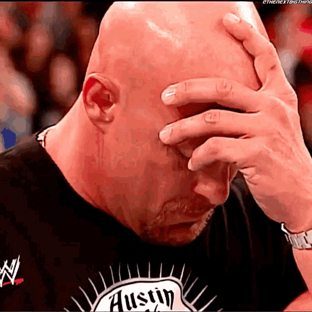 a bald man wearing an austin shirt covers his face with his hands