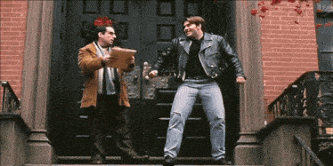 a man in a leather jacket is standing on a set of stairs talking to another man