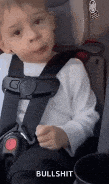 a young boy is sitting in a car seat making a funny face .