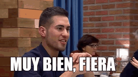 a man sitting at a table with a sign that says muy bien fiera on it