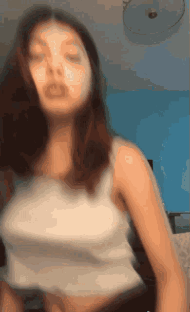 a blurry picture of a woman in a white tank top with her eyes closed