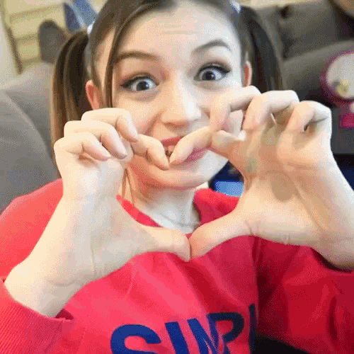 a girl in a red shirt with the word simple on it making a heart shape with her hands
