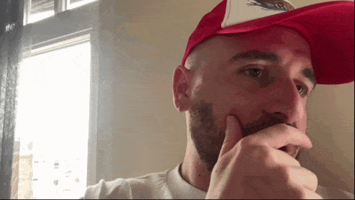 a bald man with a beard wearing a red hat with a bird on it