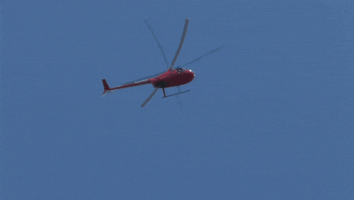a red helicopter flies through a blue sky