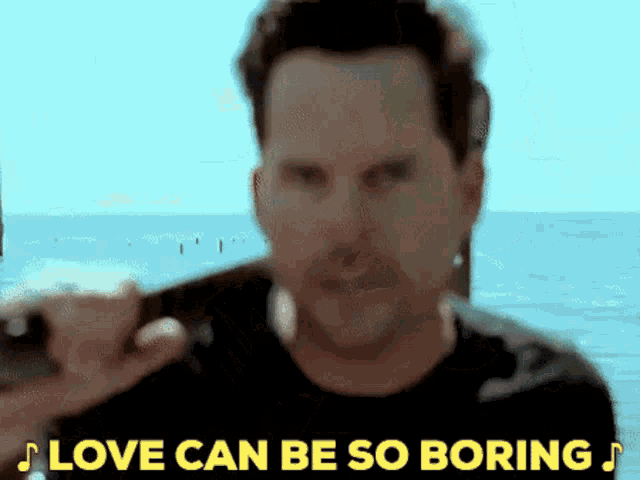 a man holding a guitar in front of the ocean with the words love can be so boring below him