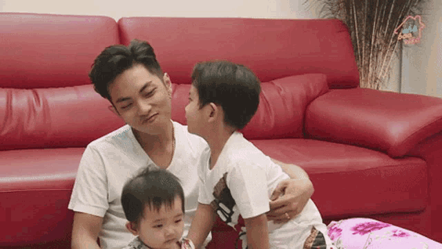 a man is sitting on a couch with two children one of whom is wearing a shirt that says adidas
