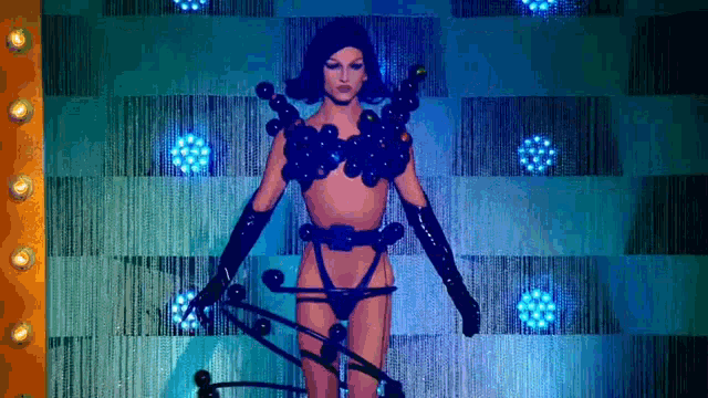 a woman in a very revealing outfit is standing in front of a blue curtain .