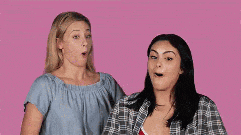 two women are standing next to each other on a pink background and one of them is making a funny face .
