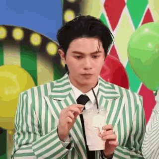 a man in a green and white striped suit and tie is holding a straw and drinking from a plastic cup .