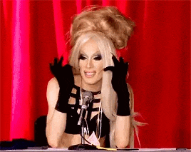 a drag queen is sitting at a table in front of a microphone wearing black gloves .