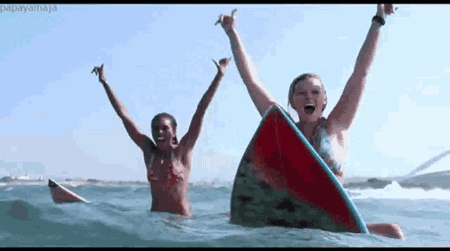 two women are surfing in the ocean with their arms in the air .