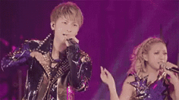 a man is singing into a microphone while standing on a stage with other people .