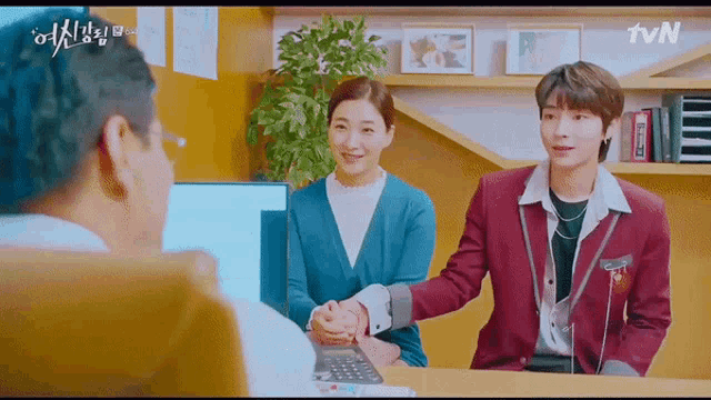 a man and a woman are shaking hands while sitting at a desk in a room .