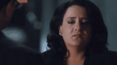 a woman in a black jacket and pearl necklace is talking to a man in a suit and glasses .