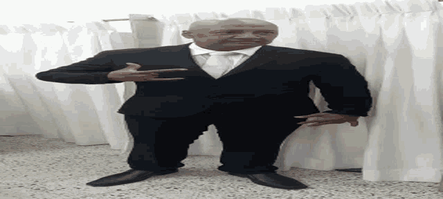 a man in a suit and tie is standing in front of white curtains