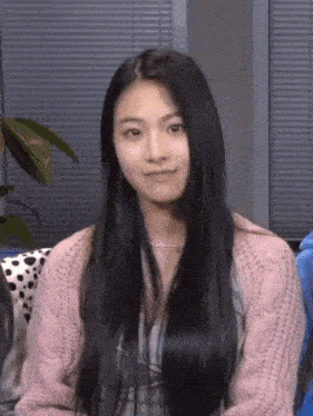 a girl with long black hair wearing a pink sweater