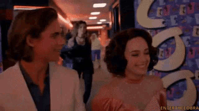 a man and a woman are smiling in a hallway with a sign that says enter the cobra on it