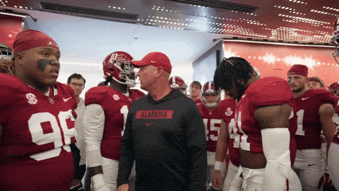 a group of alabama football players stand in a locker room with their coach