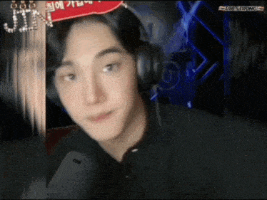 a young man wearing headphones looks at the camera with a sign that says jin on it