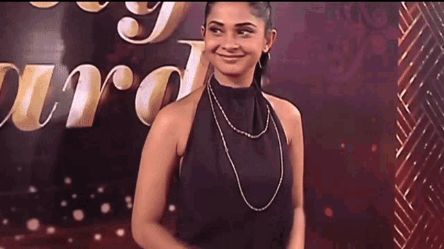 a woman wearing a black top and a necklace smiles in front of a sign that says awards