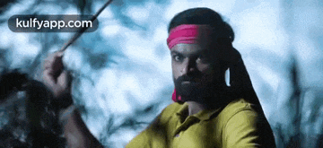 a man with a beard and a pink headband is holding a stick in his hand .
