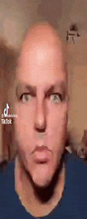 a close up of a bald man 's face with a blue shirt on making a funny face .