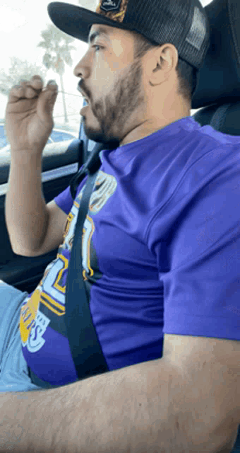 a man wearing a purple shirt and a black hat is sitting in a car