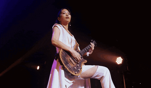 a woman in a white dress is holding a guitar with the letter g on it