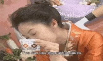 a woman in a kimono is drinking from a cup while eating vegetables .