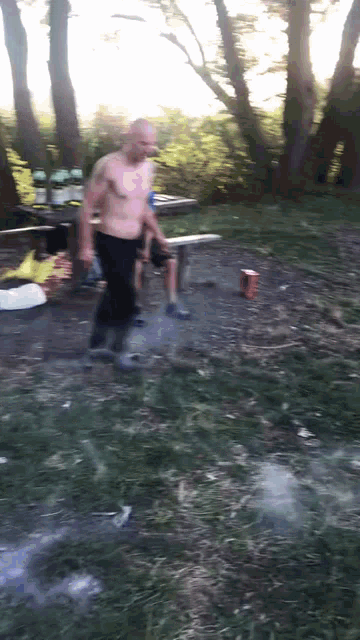 a man without a shirt is standing in a field with trees in the background