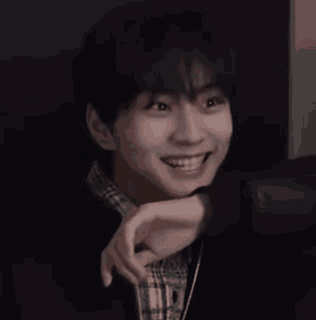 a young man is smiling and pointing at the camera while sitting in a dark room .