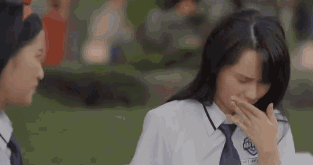 a girl in a school uniform is crying while sitting next to another girl .
