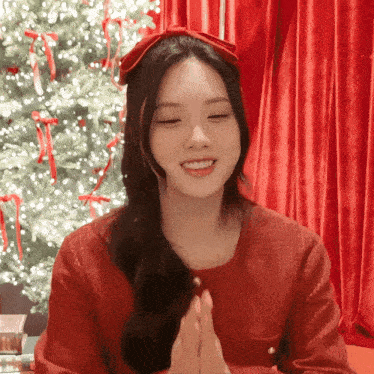 a woman wearing a red sweater and a red bow in her hair is smiling in front of a christmas tree