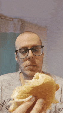 a man wearing glasses is eating a sandwich with a sticker on his shirt that says " r.o.d. "