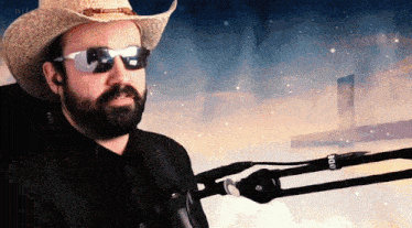 a man wearing a cowboy hat and sunglasses is in front of a rode microphone