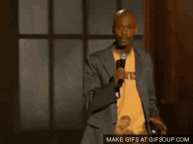 a man in a suit and yellow shirt is singing into a microphone with a make gifs at gifsoup.com watermark
