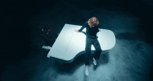 a man is sitting on a white grand piano in a dark room