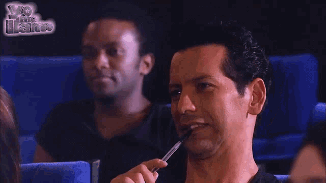 a man with a pen in his mouth is sitting in front of a sign that says yo me juro
