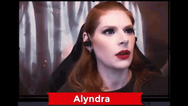 a woman with red hair is sitting in front of a monitor with the name alyndra on it