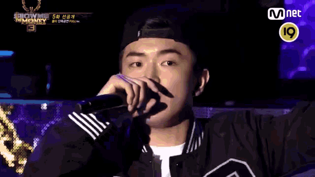 a man is singing into a microphone while wearing a hat and a black jacket .