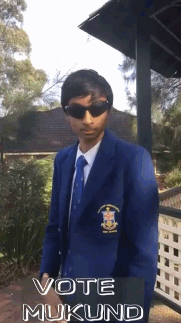 a man wearing sunglasses and a blue jacket says vote muklund